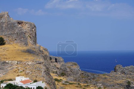 View of the white buildings of Captains houses of the 16th-18th centuries and the ancient Acropolis of Lindos in August. Lindos is an archaeological site, a fishing village. Lindos, Rhodes Island, Dodecanese, Greece  