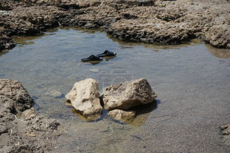Foto de Las chanclas de goma flotan en el agua de mar después de la marea baja en la costa mediterránea de Pefki. Pefkos o Pefki es un conocido balneario situado en la costa oriental de la isla de Rodas. Pefkos o Pefki, isla de Rodas, Grecia - Imagen libre de derechos