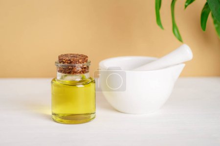 Photo for Natural cosmetic base oil and white ceramic mortar and pestle on white table on beige background. Natural cosmetics, skincare, and beauty product. Closeup. - Royalty Free Image