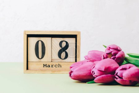 Téléchargez les photos : Bunch of purple tulips and wooden block calendar with 8 march date on a table. Womens day holiday concept, closeup. - en image libre de droit