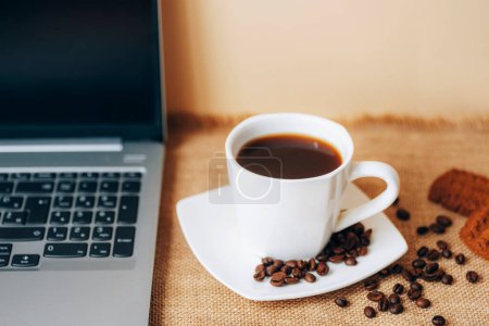 Photo for Black coffee in white cup with beans, cookies and laptop on a table. Top view, closeup. - Royalty Free Image