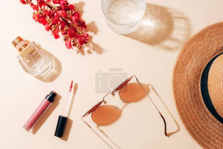 Photo for Flat lay with women's summer accessories on neutral background. Sunglasses, straw hat, lipstick, perfume bottle and red flower. Harsh shadows. Top view. - Royalty Free Image