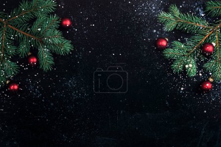 Téléchargez les photos : Branches d'arbre de Noël et boules rouges sur fond noir avec de la neige. Concept du Nouvel An. Vue du dessus, plan, espace de copie. - en image libre de droit