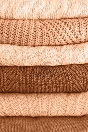 Stack of warm cozy knitted women's sweaters. Cozy autumn or winter clothes. Image toned in trendy color of year 2024 Peach Fuzz. Closeup.