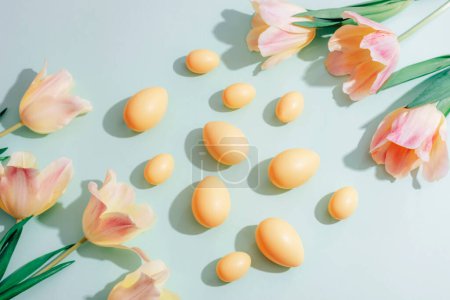 Yellow Easter eggs and tulip flowers on green background in sunlight. Easter concept. Top view, flat lay.