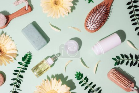 Beauty and spa accessories, cosmetics background with organic ingredients, skincare products and yellow gerbera flowers on green background with sharp shadows. Top view, flat lay.