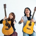 Portrait of Asian duo artists with an acoustic guitar sitting on a white background and show the gesture of thumps up for music, artist, musician concept
