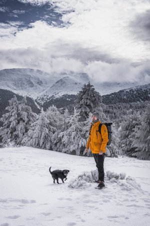 Téléchargez les photos : Une personne en manteau jaune et un chien noir frappant une pose au milieu d'un paysage enneigé pittoresque, mettant en valeur la beauté de leur compagnie. - en image libre de droit