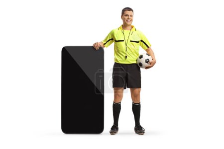 Foto de Retrato completo de un árbitro de fútbol de pie junto a un gran smartphone aislado sobre fondo blanco - Imagen libre de derechos