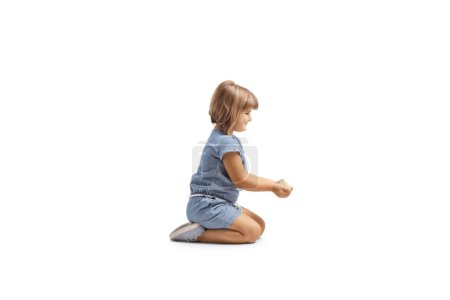Foto de Perfil de una niña pequeña sosteniendo comida de grano en sus manos y arrodillada aislada sobre fondo blanco - Imagen libre de derechos