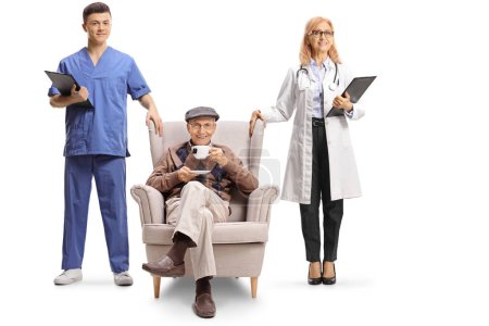 Photo for Female doctor and male nurse standing next to an elderly man in an armchair with a cup of tea isolated on white background - Royalty Free Image