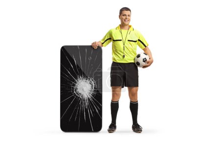 Foto de Retrato completo de un árbitro de fútbol de pie junto a un smartphone con pantalla rota aislada sobre fondo blanco - Imagen libre de derechos