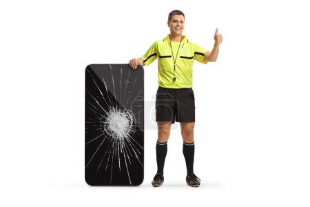Foto de Retrato completo de un árbitro de fútbol con un smartphone con pantalla rota que muestra los pulgares hacia arriba aislados sobre fondo blanco - Imagen libre de derechos