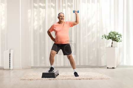 Photo for Full length portrait of a mature man exercising step aerobic with a small weight at home - Royalty Free Image