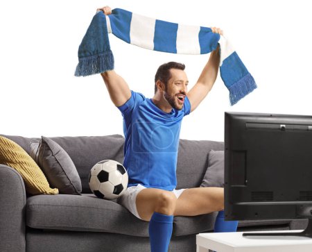 Foto de Hombre alegre en una camiseta de fútbol animando con una bufanda y sentado en un sofá delante de un televisor aislado sobre fondo blanco - Imagen libre de derechos