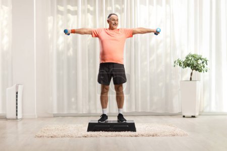 Photo for Full length portrait of a mature man exercising step aerobic and holding weights indoors - Royalty Free Image