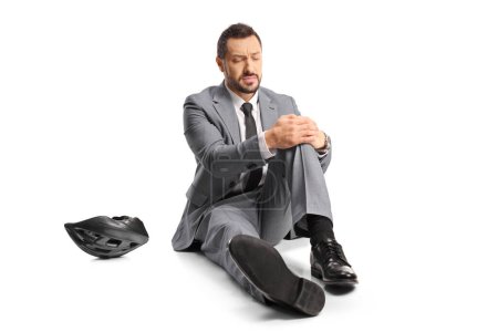 Téléchargez les photos : Homme d'affaires assis sur le sol et tenant son genou douloureux isolé sur fond blanc - en image libre de droit