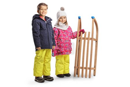 Foto de Niños con ropa de invierno de pie con un trineo de madera aislado sobre fondo blanco - Imagen libre de derechos