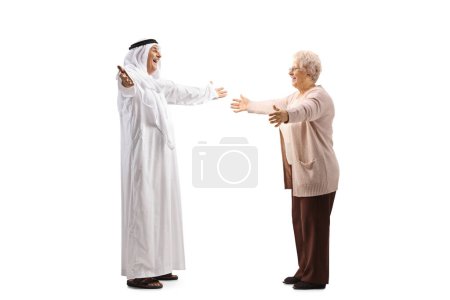 Foto de Foto de perfil completo de un hombre árabe maduro en una bata saludando a una anciana aislada sobre fondo blanco - Imagen libre de derechos