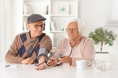 Foto de Mujer mayor revisando la presión arterial a un hombre mayor en casa - Imagen libre de derechos