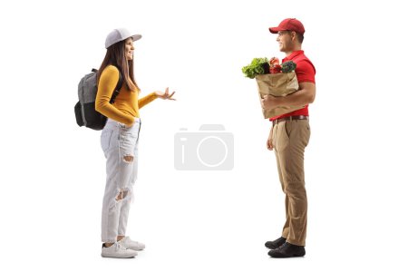 Photo for Full length profile shot of a female student with a backpack talking to a delivery man with a grocery bag isolated on white background - Royalty Free Image