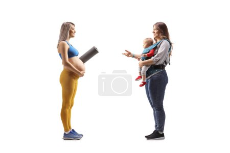 Foto de Foto de perfil completo de una mujer embarazada en ropa deportiva con una esterilla de ejercicio teniendo una conversación con una madre y un bebé aislados sobre fondo blanco - Imagen libre de derechos