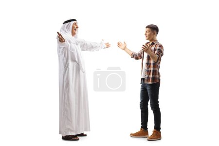 Foto de Foto de perfil completo de un hombre árabe maduro en una bata saludando a un joven hombre casual aislado sobre fondo blanco - Imagen libre de derechos