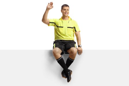 Foto de Retrato de longitud completa de un árbitro de fútbol sentado en un panel en blanco y saludando aislado sobre fondo blanco - Imagen libre de derechos