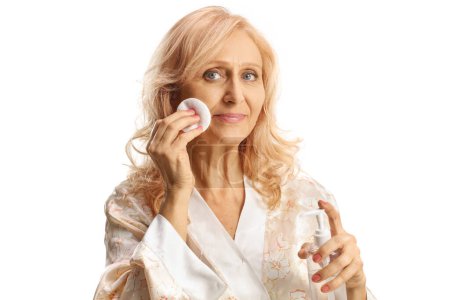 Téléchargez les photos : Femme mûre nettoyant son visage avec un coton isolé sur fond blanc - en image libre de droit