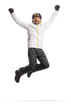 Téléchargez les photos : Jeune homme portant un manteau d'hiver et un casque de ski et sautant d'un geste de bonheur isolé sur fond blanc - en image libre de droit