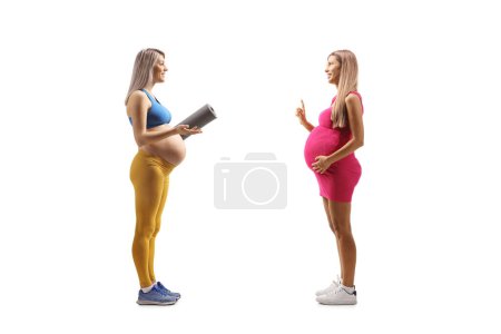 Téléchargez les photos : Femme enceinte en tenue de sport avec un tapis d'exercice ayant une conversation avec une autre femme enceinte isolée sur fond blanc - en image libre de droit
