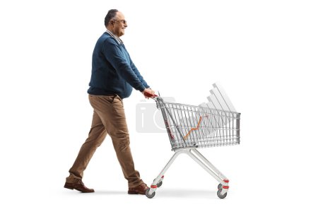 Photo for Full length profile shot of a mature man walking and pushing a shopping cart with a bar chart isolated on white background - Royalty Free Image