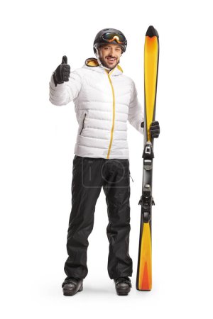 Photo for Full length portrait of a man with a pair of skiis showing thumbs up and smiling isolated on white background - Royalty Free Image