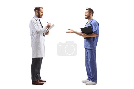 Foto de Foto de perfil completo de un médico varón de pie y escribiendo un documento y hablando con un trabajador sanitario aislado sobre fondo blanco - Imagen libre de derechos