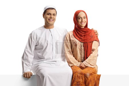 Photo for Young couple in ethnic clothing sitting on a white panel isolated on white background - Royalty Free Image