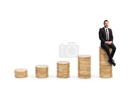 Foto de Montones crecientes de monedas y hombre de negocios sentado en la parte superior aislado sobre fondo blanco - Imagen libre de derechos