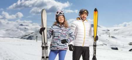 Foto de Joven pareja de esquiadores con cascos y gafas posando en una montaña - Imagen libre de derechos