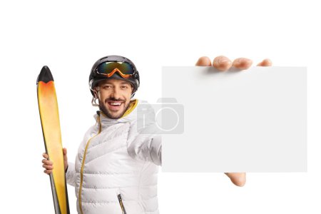 Photo for Male skier holding skiis and showing a small blank cardboard isolated on white background - Royalty Free Image