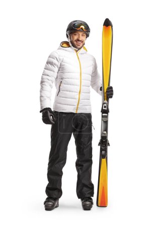 Photo for Full length portrait of a male skier with equipment standind and holding a pair of skis isolated on white backgroun - Royalty Free Image