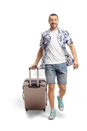 Téléchargez les photos : Portrait complet d'un homme souriant marchant et tirant une valise isolée sur fond blanc - en image libre de droit