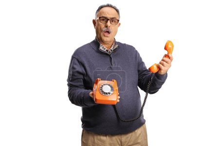 Photo for Angry mature man holding a vintage rotary phone and looking at camera isolated on white background - Royalty Free Image