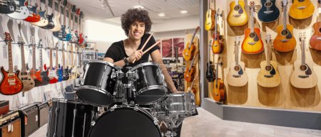 Foto de Joven sonriente sosteniendo palos de batería y sentado con un tambor dentro de una tienda de música - Imagen libre de derechos