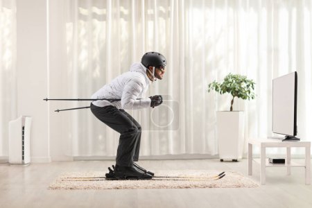 Photo for Profile shot of a man skiing at home in a living room in front of  t - Royalty Free Image