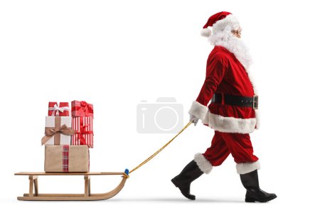 Photo for Full length profile shot of santa claus pulling a wooden sled with presents isolated on white background - Royalty Free Image