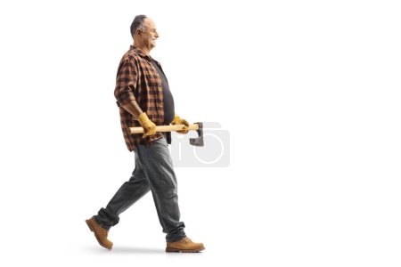 Téléchargez les photos : Plan de profil complet d'un homme mature marchant et tenant une hache isolée sur fond bleu - en image libre de droit