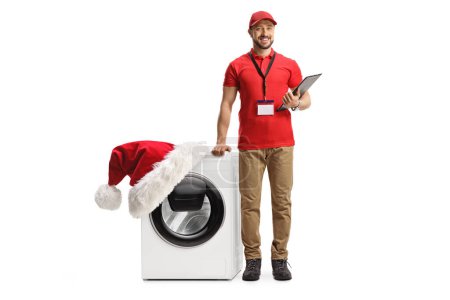 Photo for Full length portrait of a shop assitant leaning on a washing machine decorated with a santa claus hat isolated on white background - Royalty Free Image