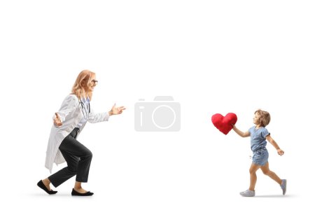 Foto de Foto de perfil de una doctora esperando para abrazar a una niña llevando un corazón rojo aislado sobre fondo blanco - Imagen libre de derechos