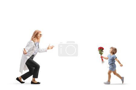 Téléchargez les photos : Petite fille tenant des roses rouges et courant vers une femme médecin isolée sur fond blanc - en image libre de droit