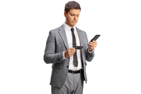 Photo for Young professional man holding a smartphone and looking at a credit card isolated on white background - Royalty Free Image