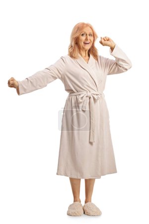 Photo for Full lenght shot of a mature woman in a bathrobe stretching and yawning isolated on white background - Royalty Free Image